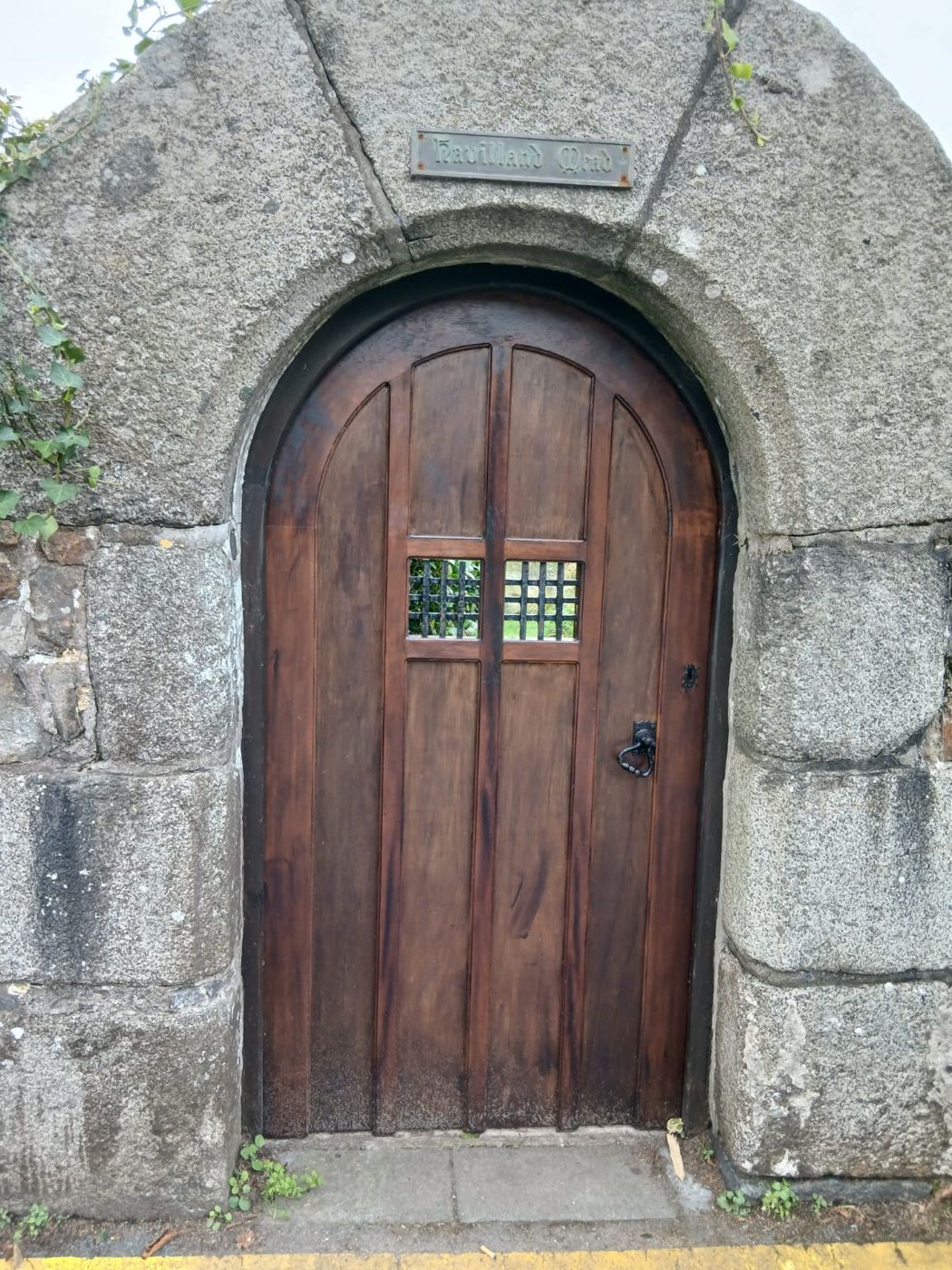Front view of the finished arched door restored by Le Foulon Joinery, with iron grilles and ring handle set in a granite arch