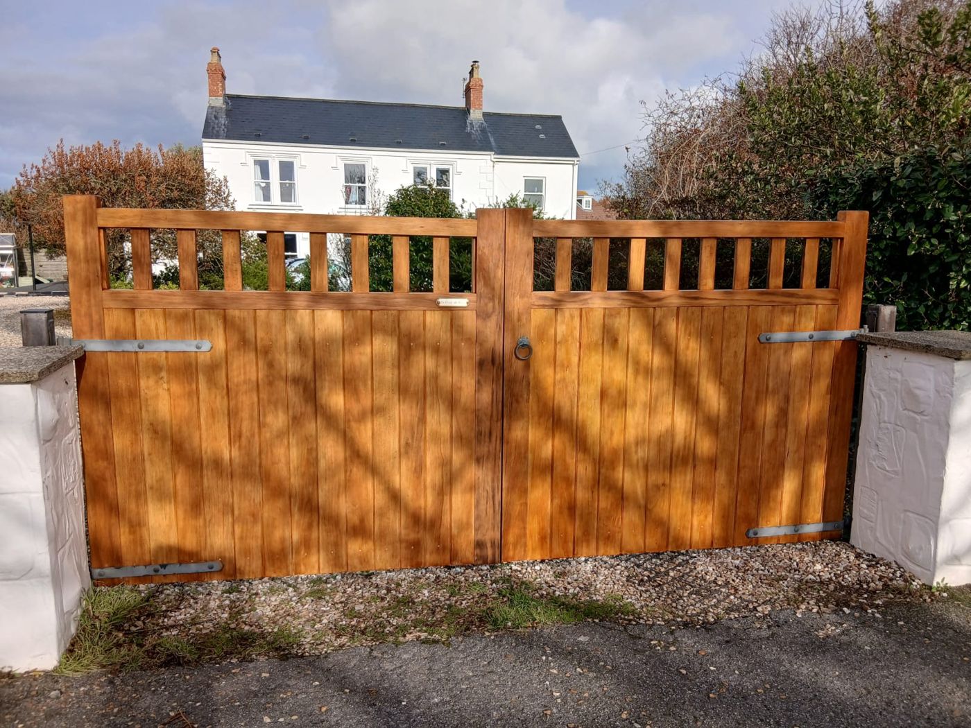 Pair of timber driveway gates with slatted top rails and iron strap hinges between white pillars, made by Le Foulon Joinery